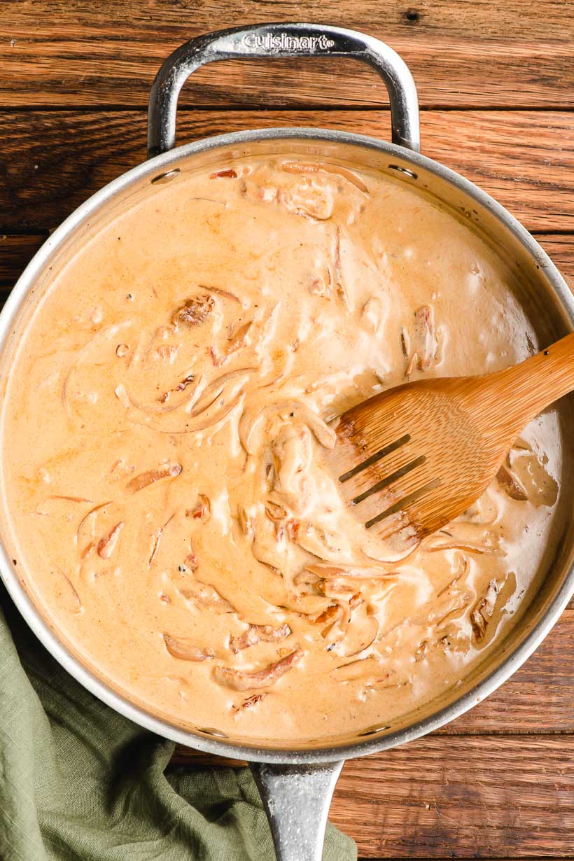 Creamy sun dried tomato sauce in a deep skillet being stirred with a wooden spoon.