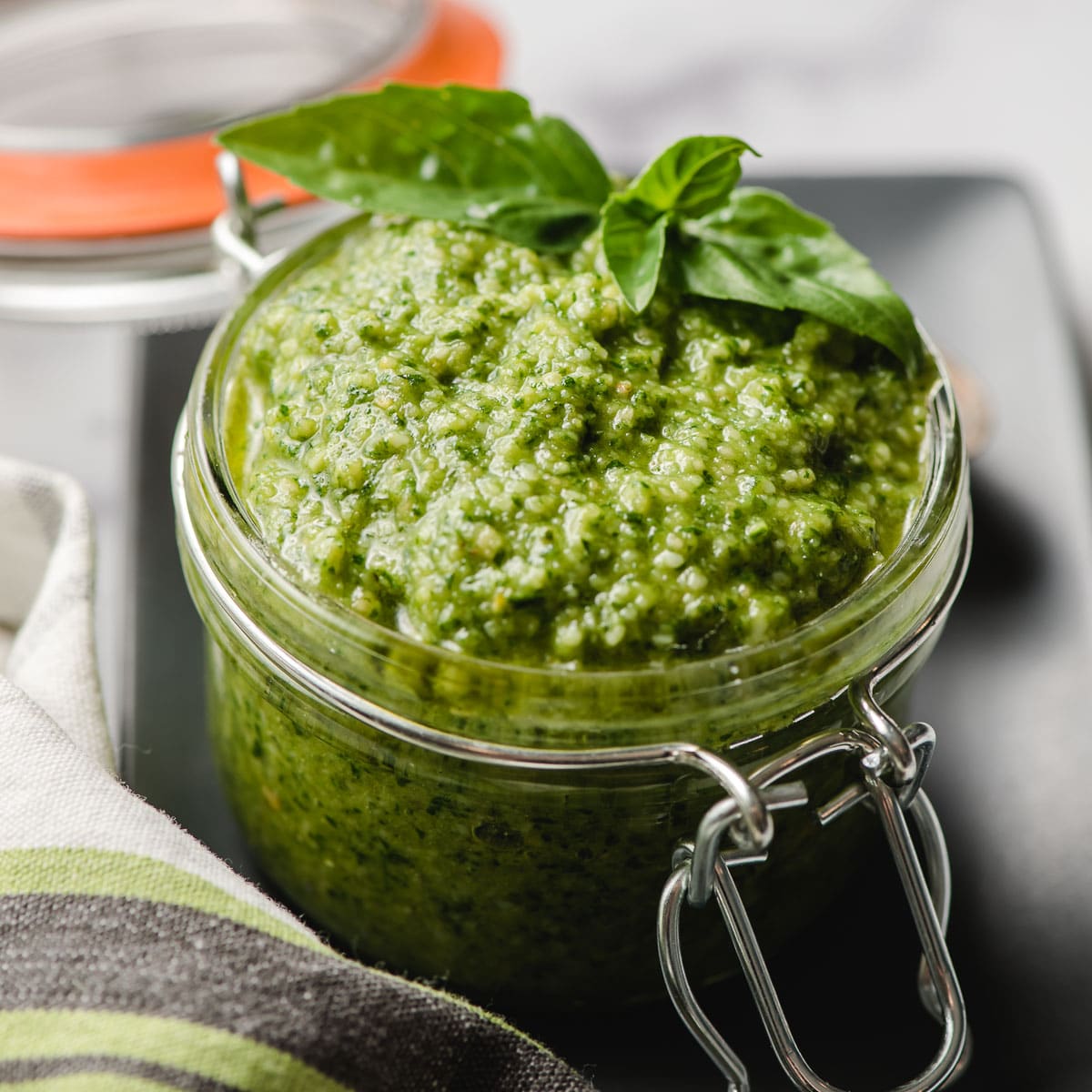 Jarred pesto garnished with fresh basil sprig.