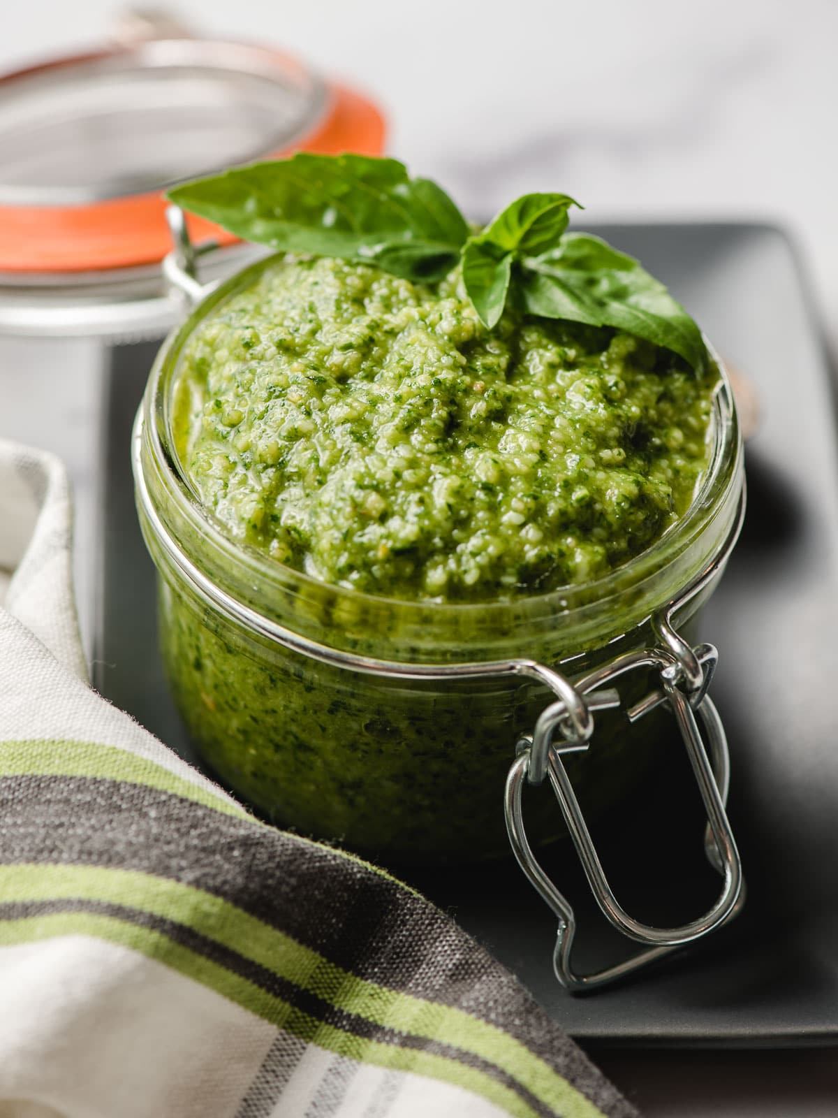 Small glass jar filled to overflowing with fresh basil pesto.