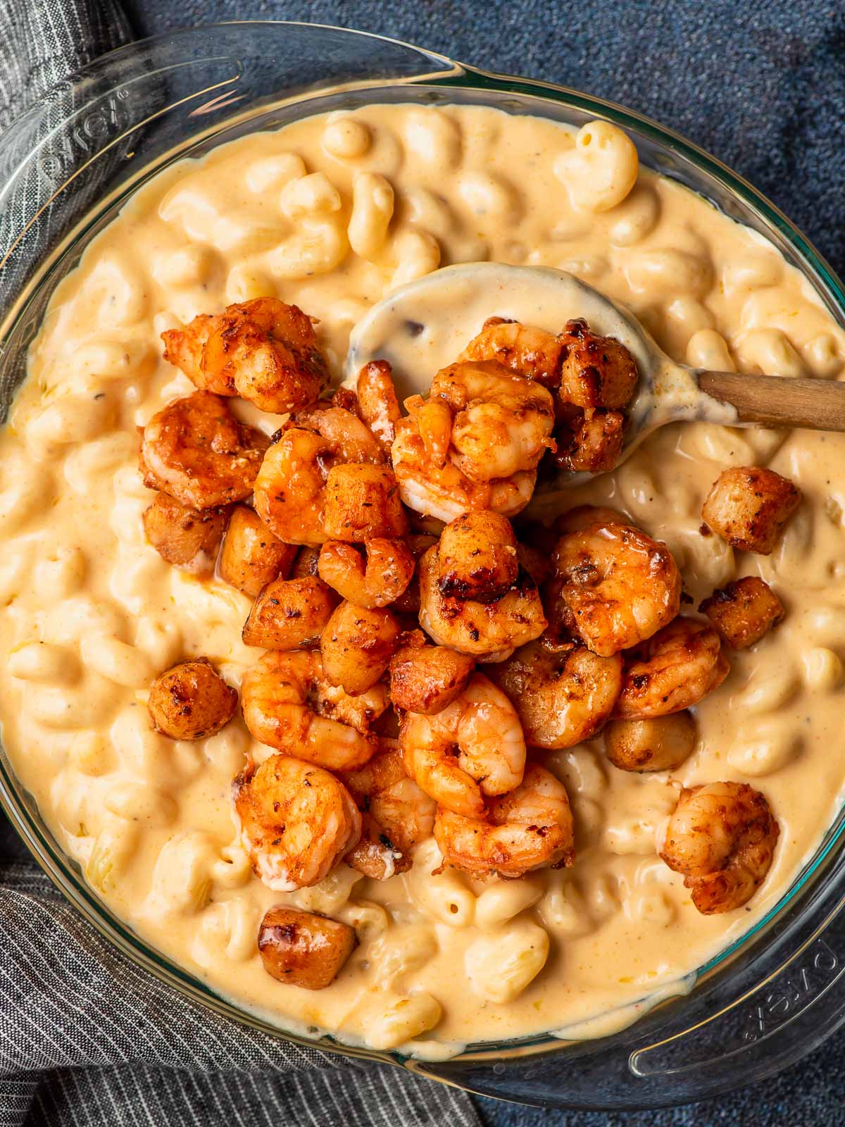 Creamy mac and cheese shown in a glass casserole dishwith seasoned shrimp and scallops on top.