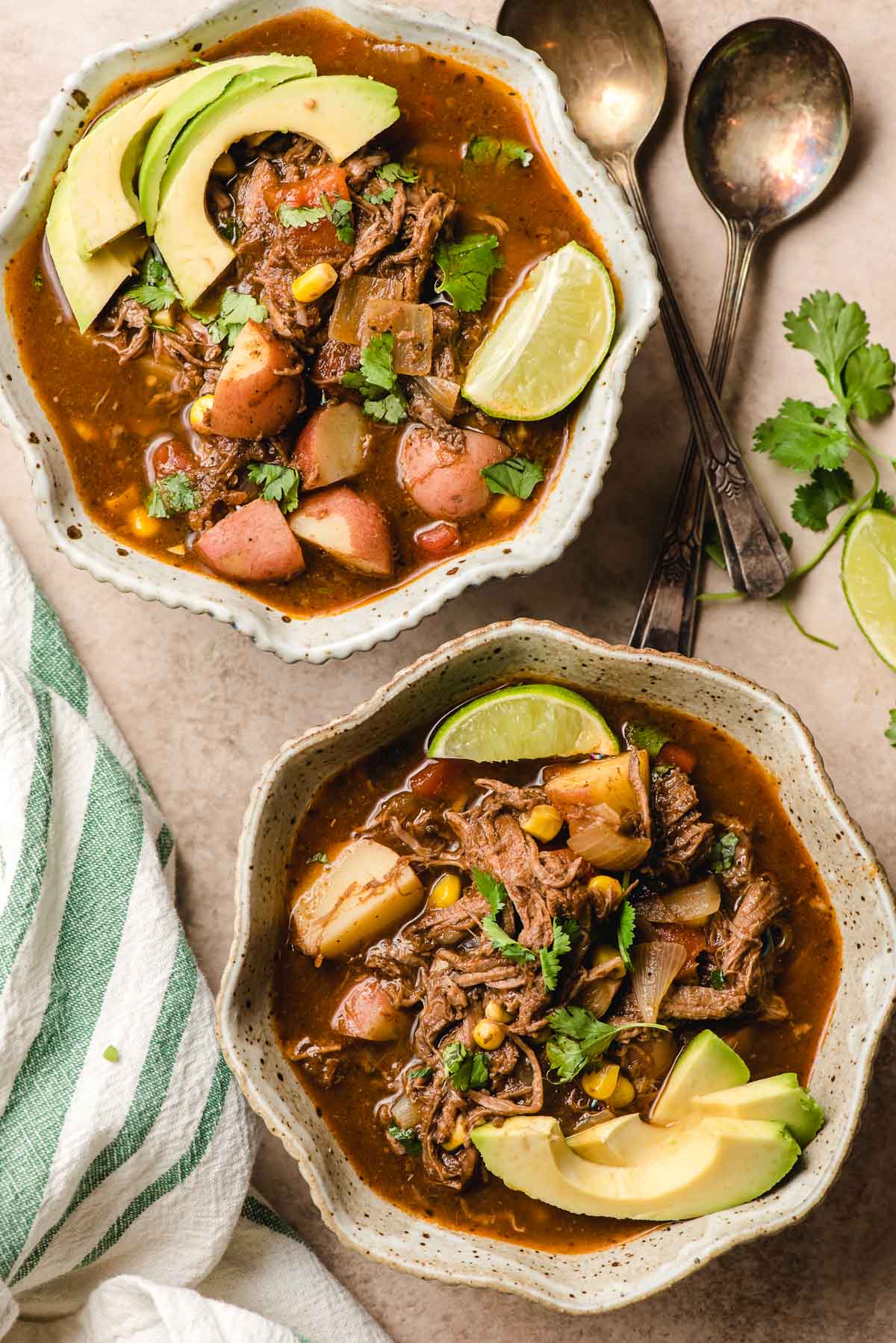 Two bowls of Mexican Beef Stew on a speckled beige background with cilantro sprigs.