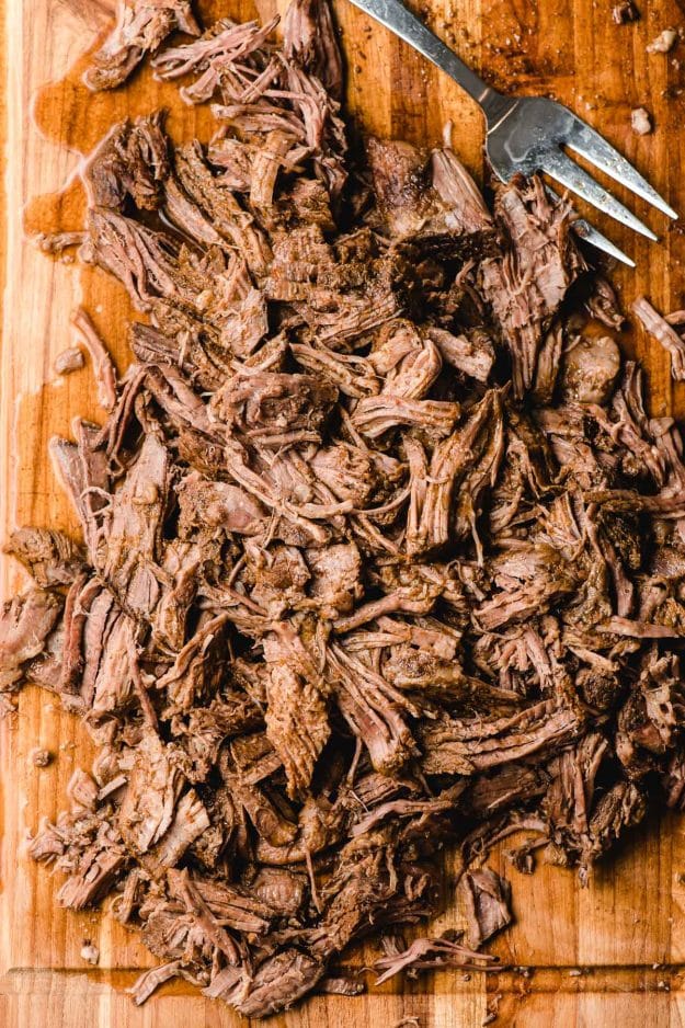 Shredded barbacoa beef on a wood cutting board.