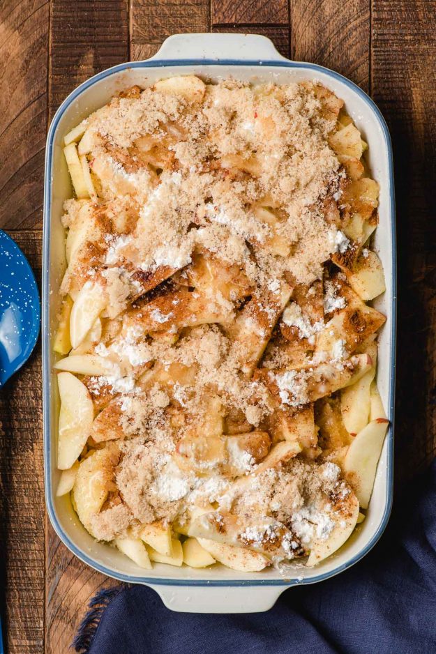 Apple slices in a blue rimmed white casserole dish topped with cinnamon and sugar.