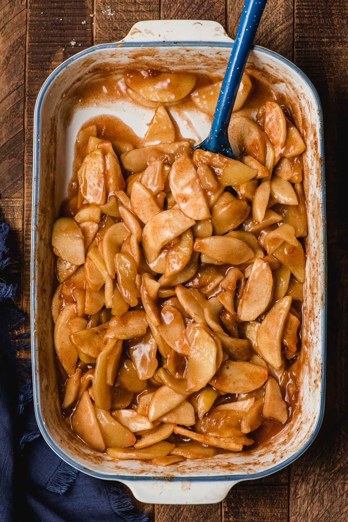 Spoon scooping cinnamon baked apples out of a white casserole dish.