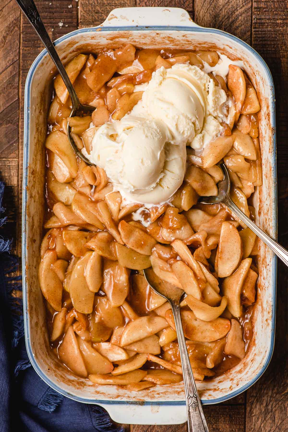 Casserole dish full of baked apples with three spoons and two scoops of ice cream on top.