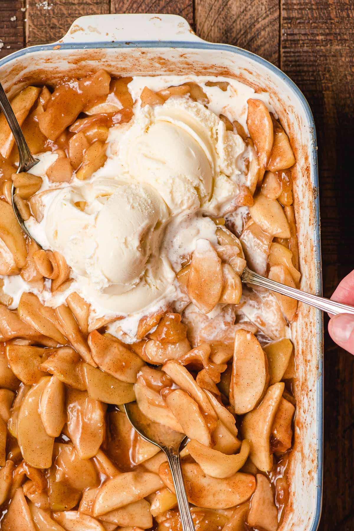 Spoon taking a big bite out of a dish of cinnamon baked apples with pools of melted ice cream.