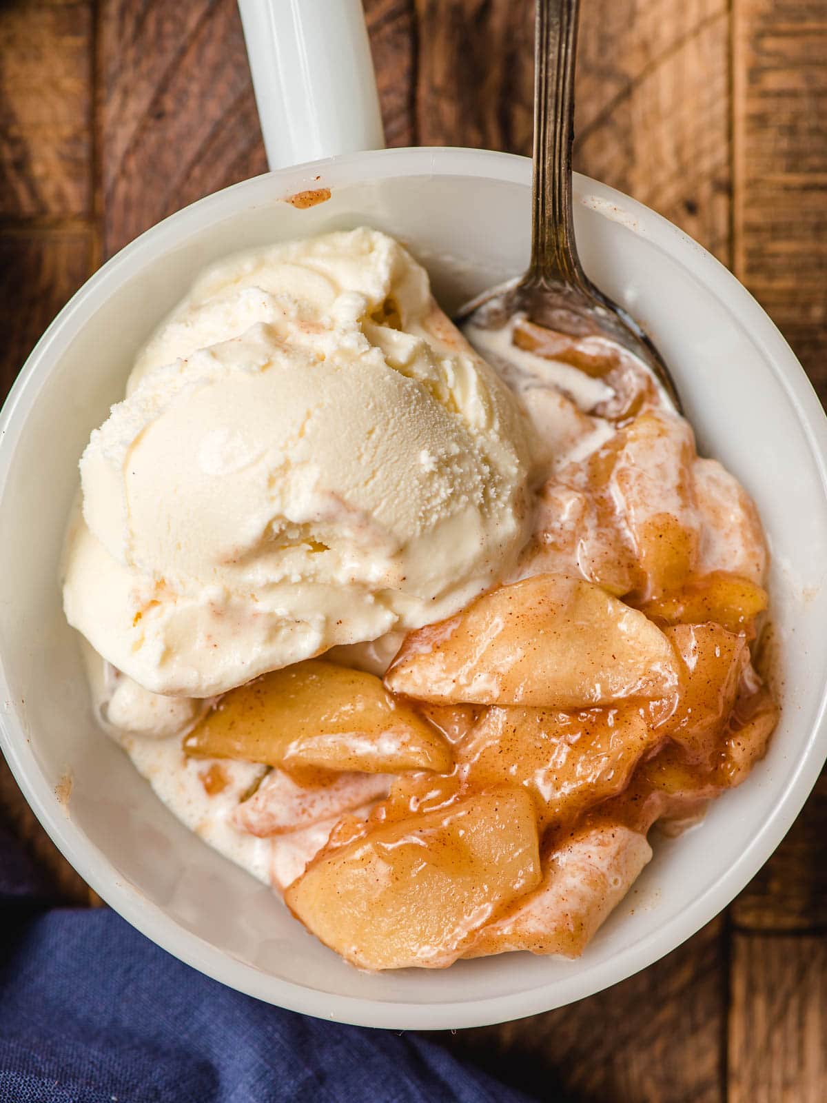 White bowl filled with warm cinnamon apples and a scoop of vanilla ice cream.