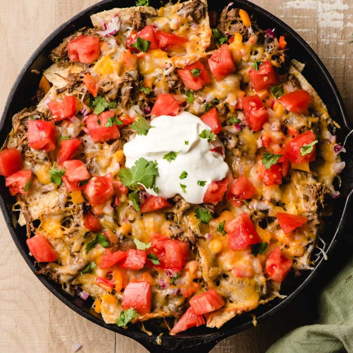 Cast Iron Skillet Nachos topped with beef, cheese, tomatoes, onions, sour cream, and cilantro.