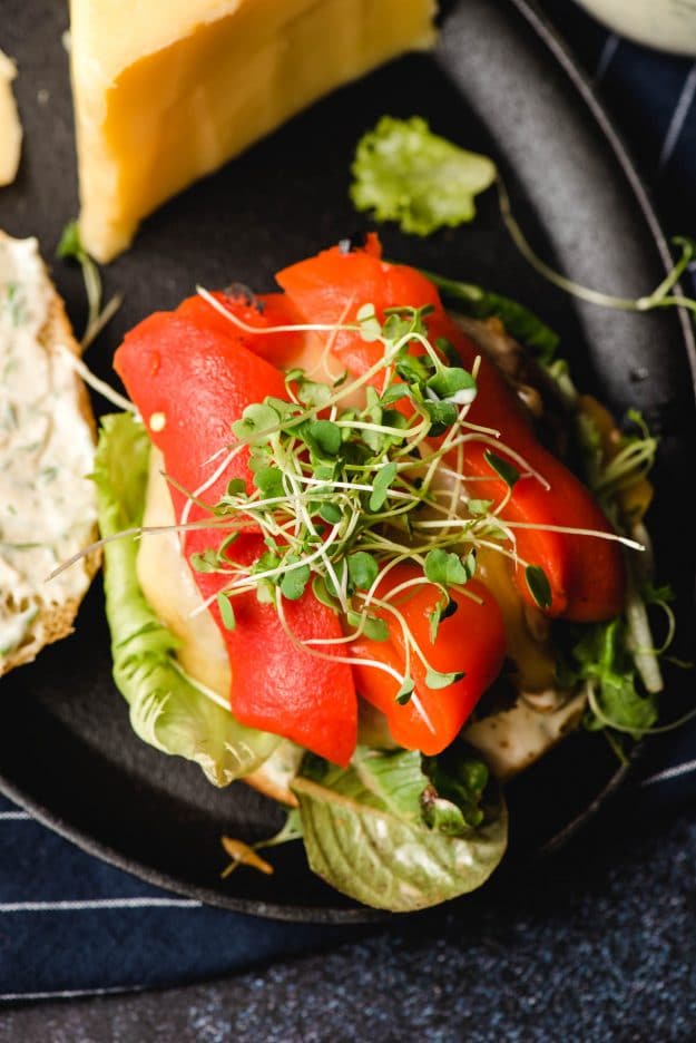 Open face portobello sandwich topped with roasted red pepper slices and microgreens.