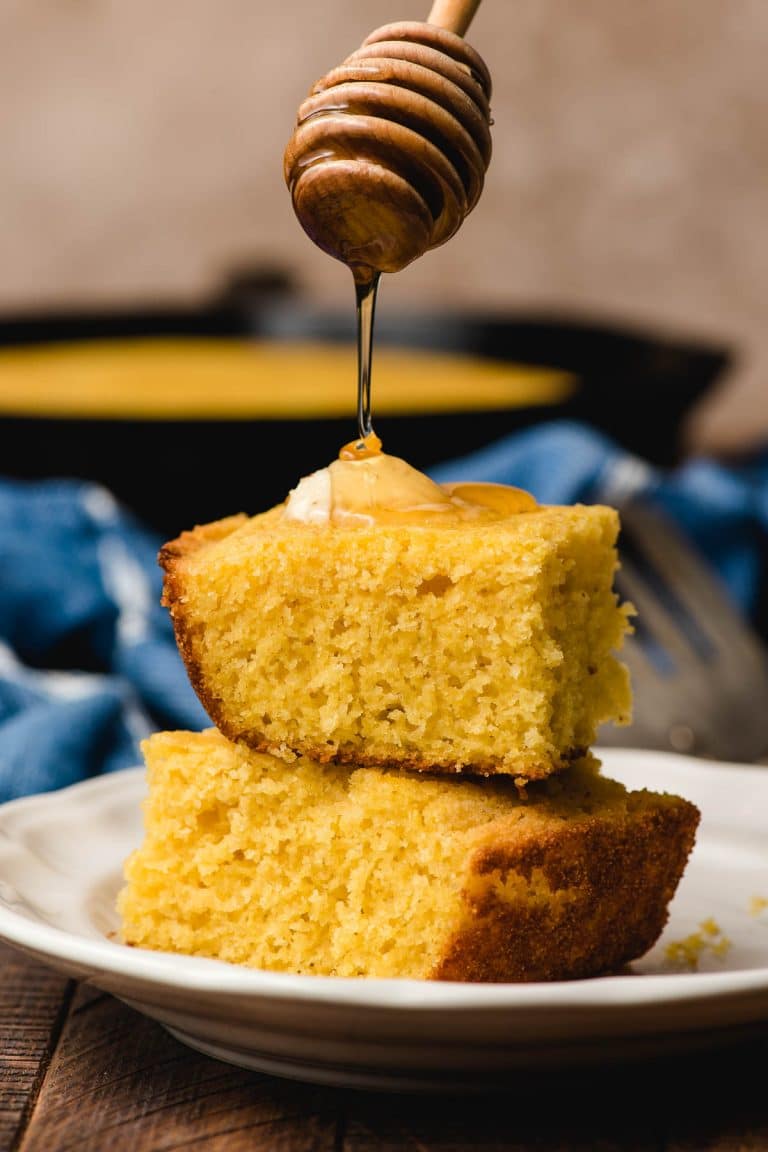 Honey dipper drizzling honey on a stack of cornbread slices.