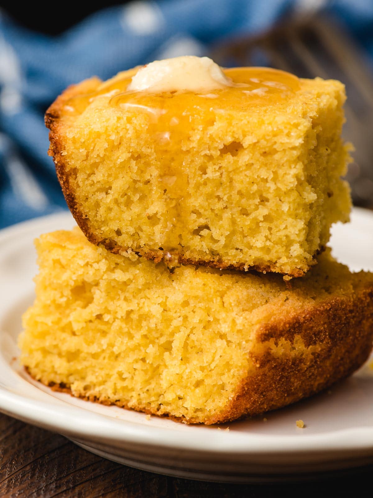 A stack of two slices of cornbread with a pat of butter on top and honey dripping down the side.