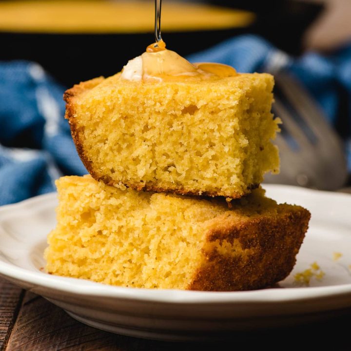 Two slices of cornbread stacked on top of each other with a drizzle of honey on top.