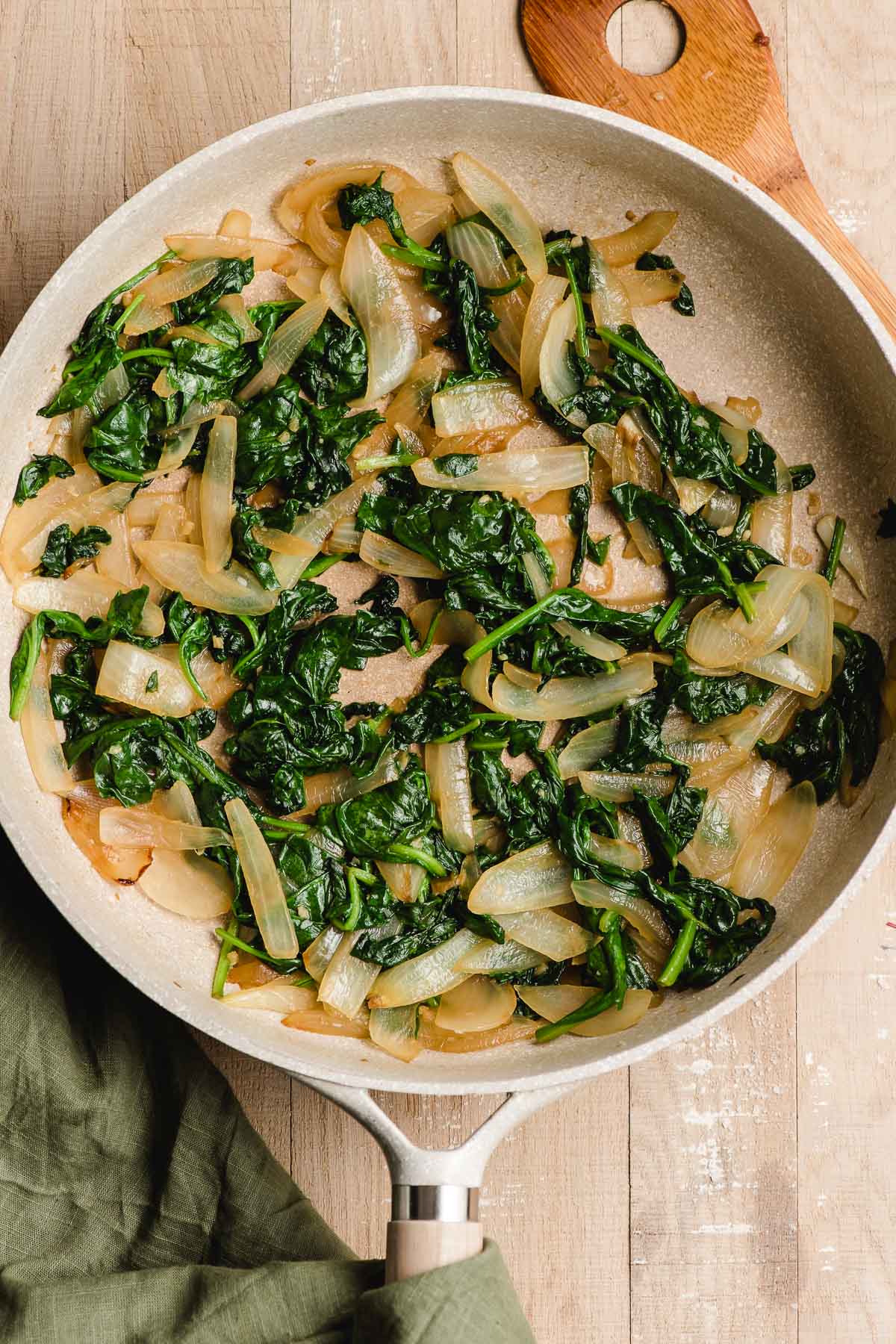 Skillet holding cooked spinach and browned onions.