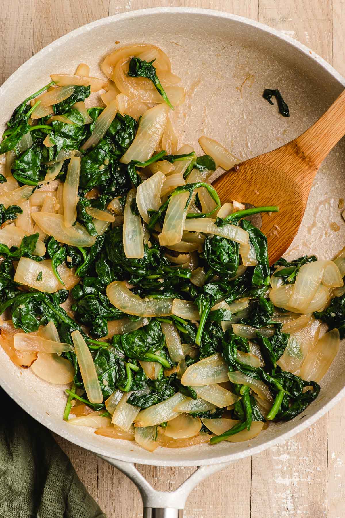 Speckled beige skillet with sauteed spinach and onions.