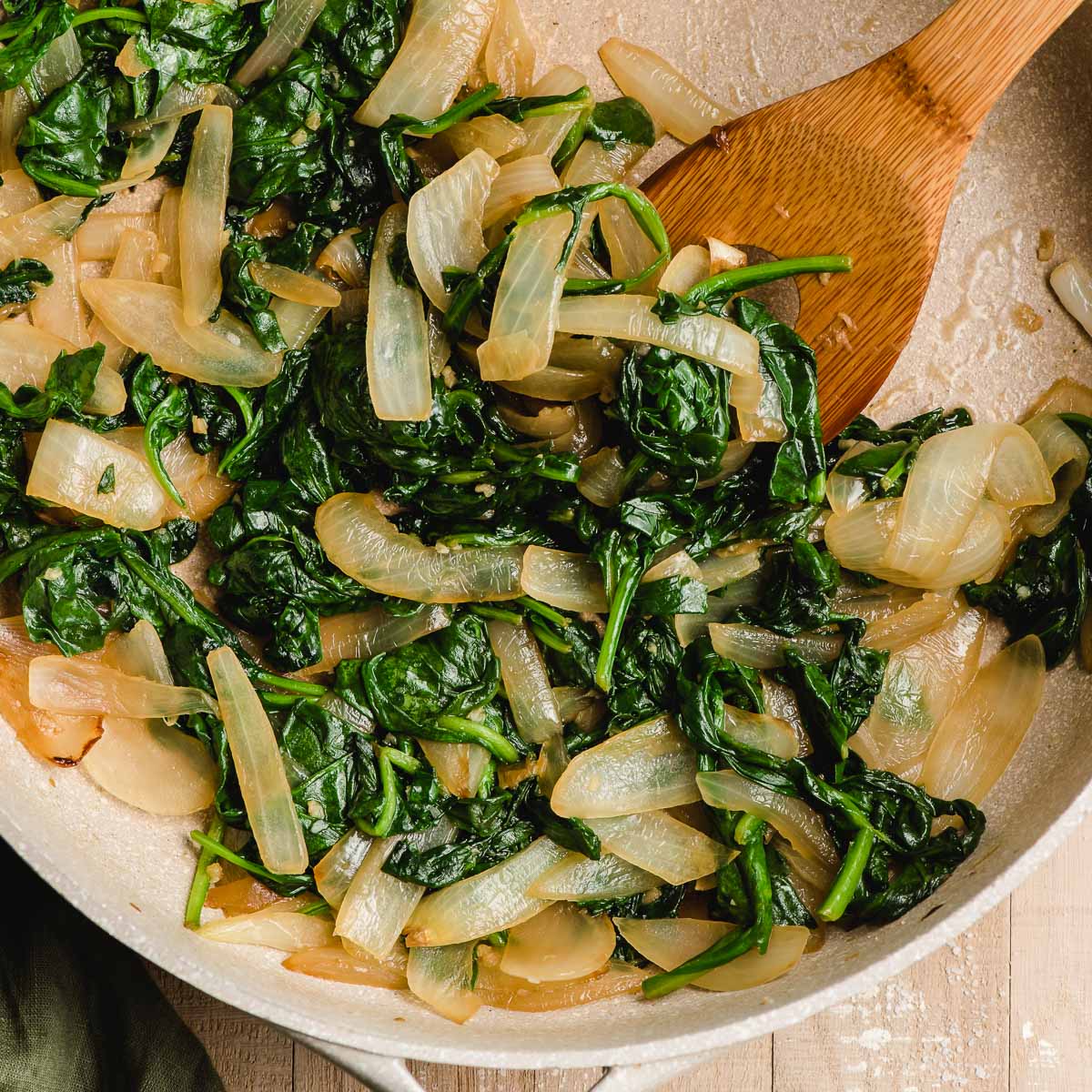 Sauteed spinach and onions in a skillet with a wooden spoon.