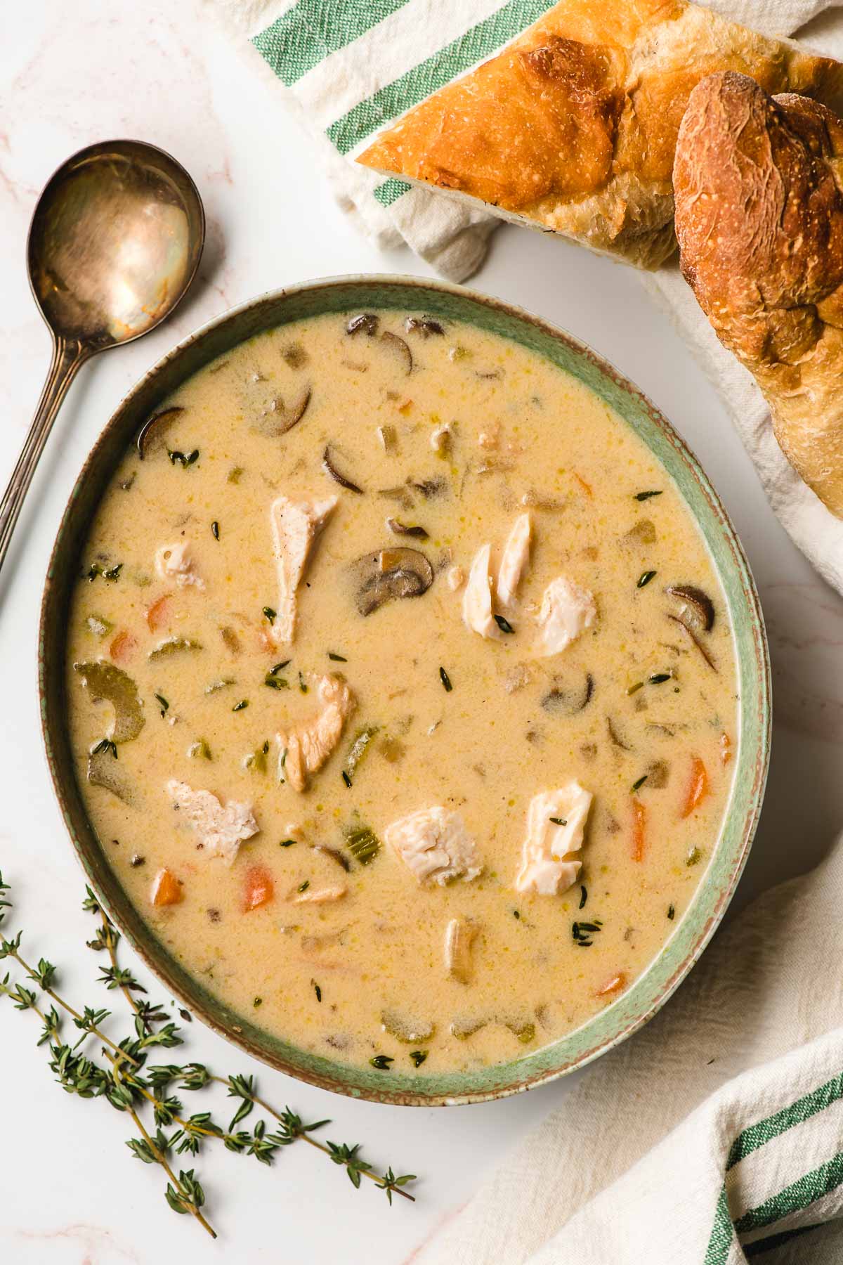 Bowl of Creamy Turkey Soup surrounded by thyme leaves and two hunks of crust French bread.