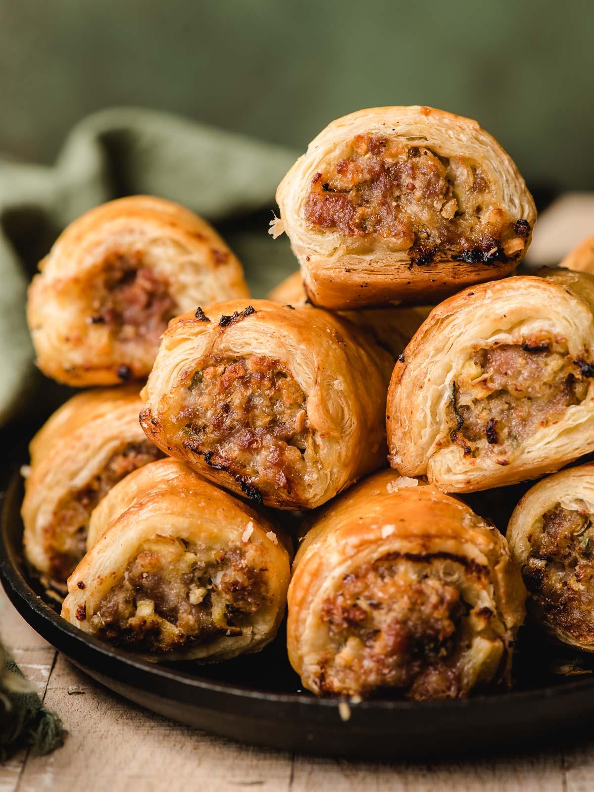 Pile of puff pastry sausage rolls on a cast iron serving platter.