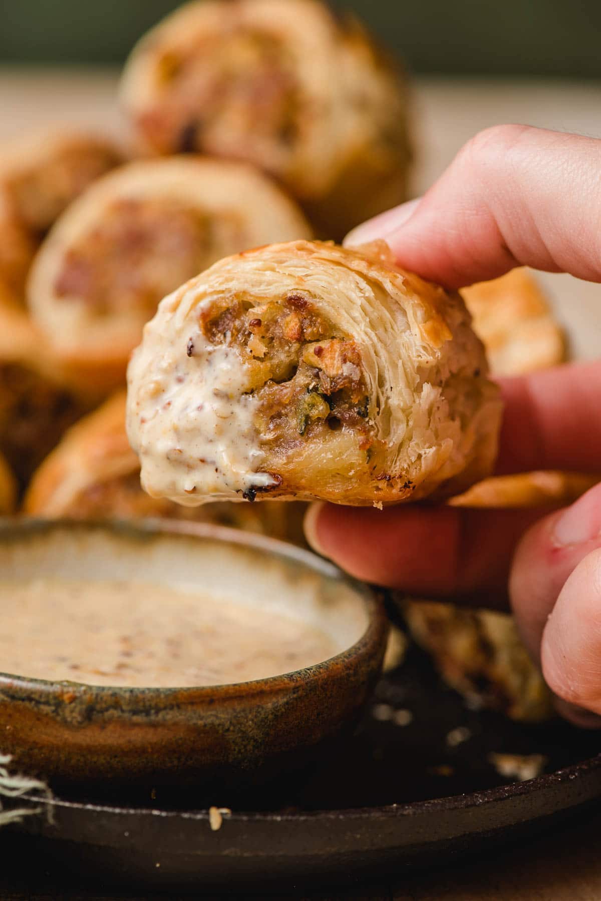 Sausage roll dipped in a bowl of mustard sauce.
