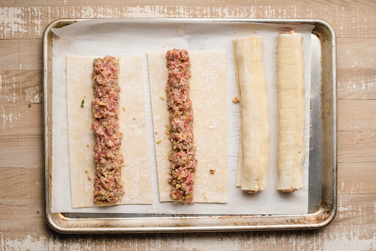 Four unbaked sausage logs on a baking sheet.