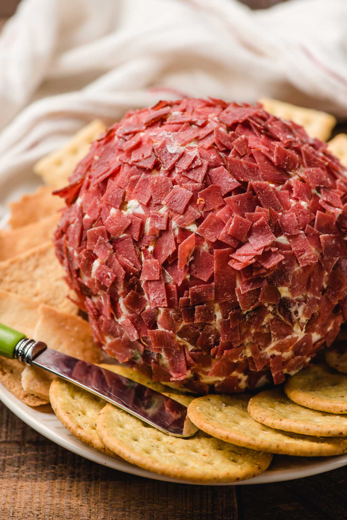 Cheeseball with chipped beef on a plate with crackers and a cheese knife.