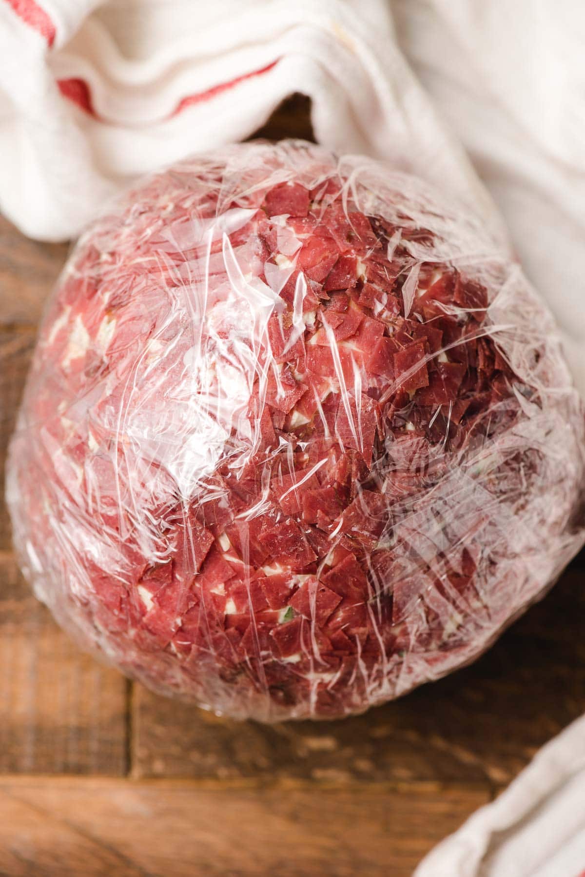 Cheeseball with dried beef wrapped in saran wrap to prepare for freezing.