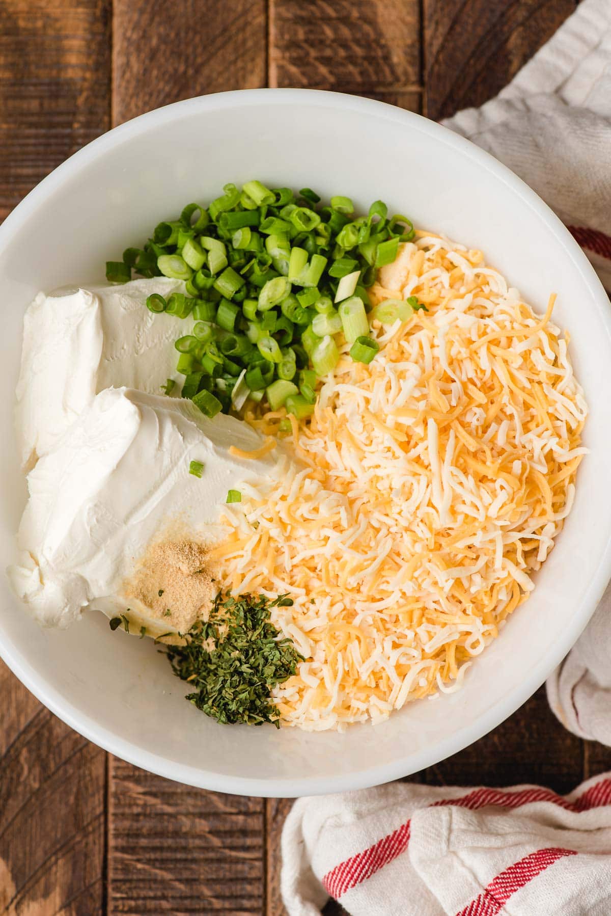 White bowl filled with ingredients for a cheese ball-softened cream cheese, shredded cheese, green onions, garlic powder, parsley, and Worcestershire.
