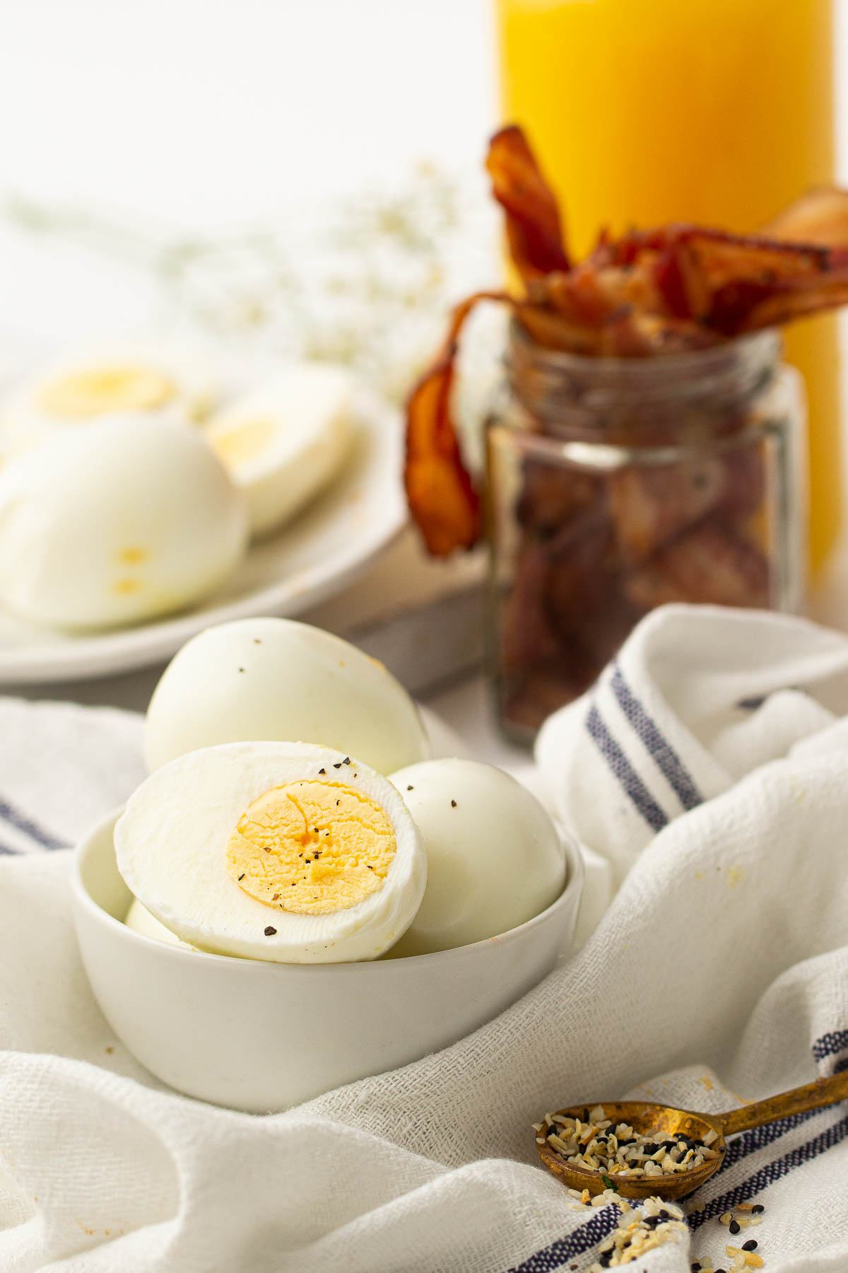 Air fryer hard boiled eggs shown in a white bowl, with a cup of cooked bacon slices in the background.