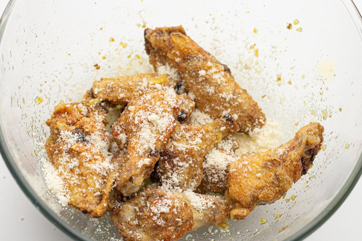 Chicken wings tossed with butter, garlic, and grated Parmesan cheese in a mixing bowl.