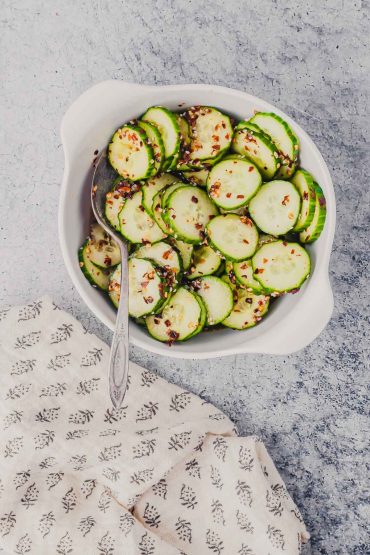 Cucumbers in a white bowl seasoned with red pepper flakes, salt, sugar, and vinegar.