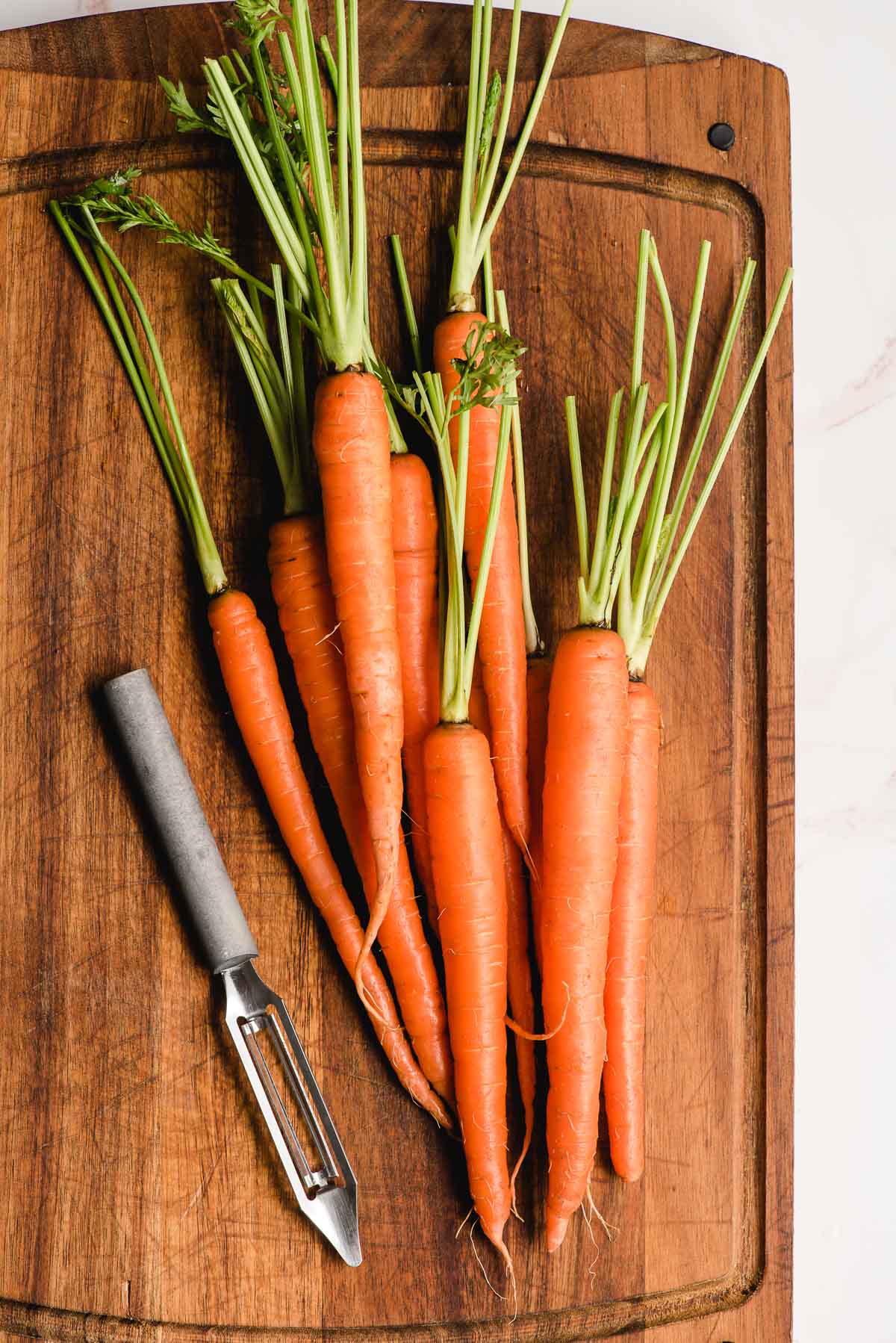 Fresh carrots on a cutting board with a vegetable peeler.