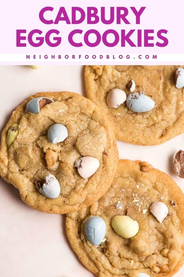 Three Cadbury mini egg cookies on a pale pink background.