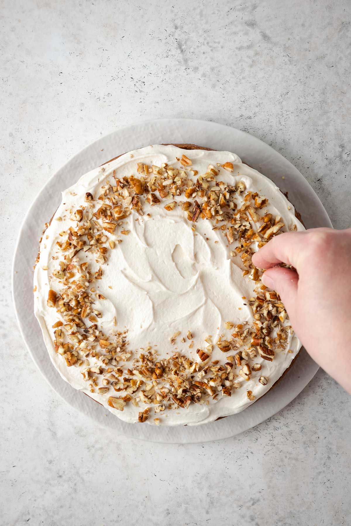 Hand sprinkling walnuts onto a frosted gluten free carrot cake.