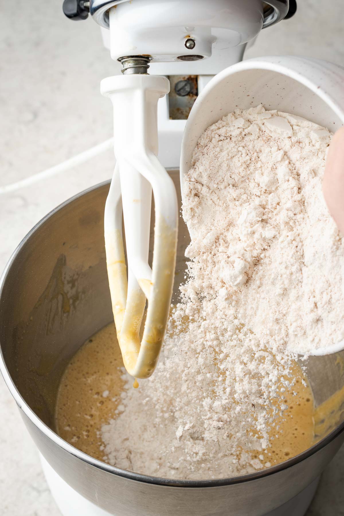 Pouring dry ingredients into cake batter in a stand mixer.