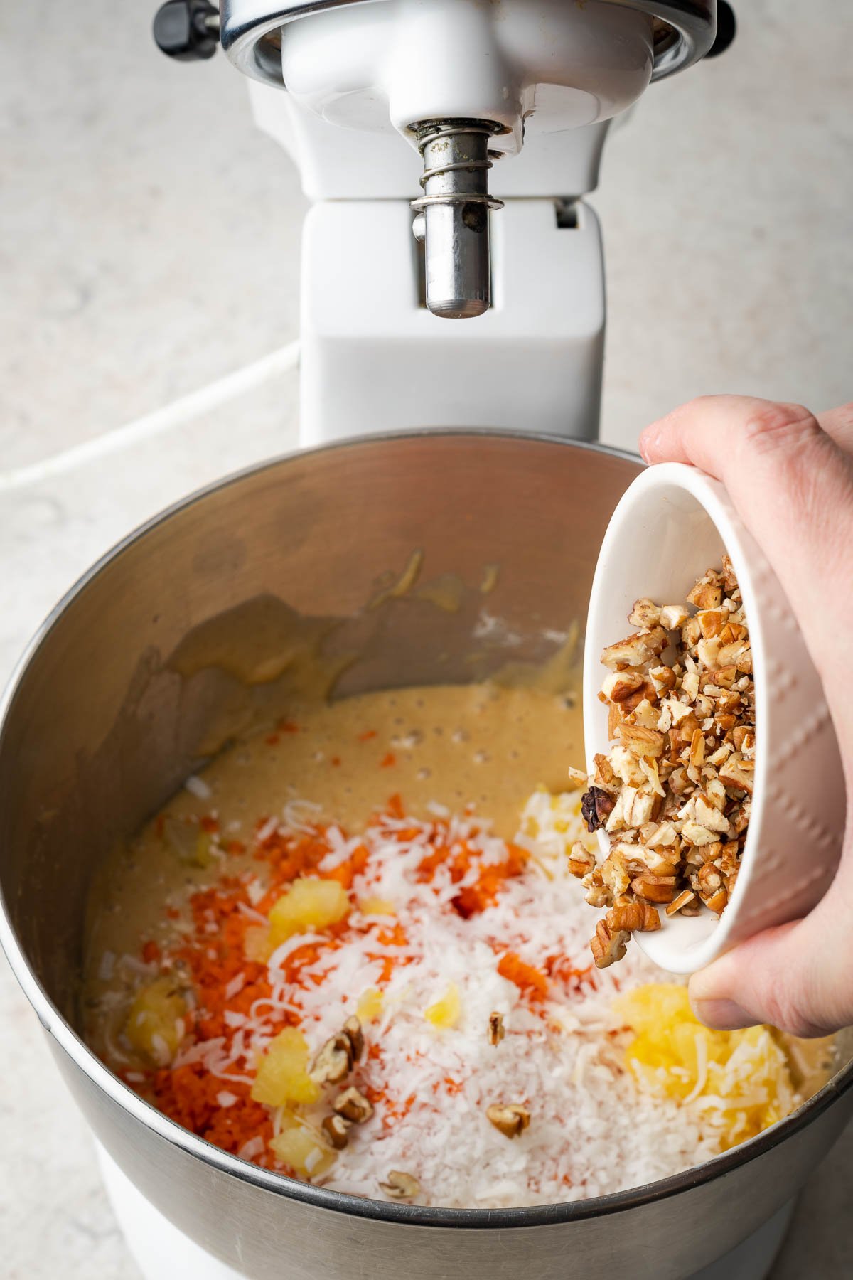 Pouring pineapple, carrots, coconut, and walnuts into cake batter.