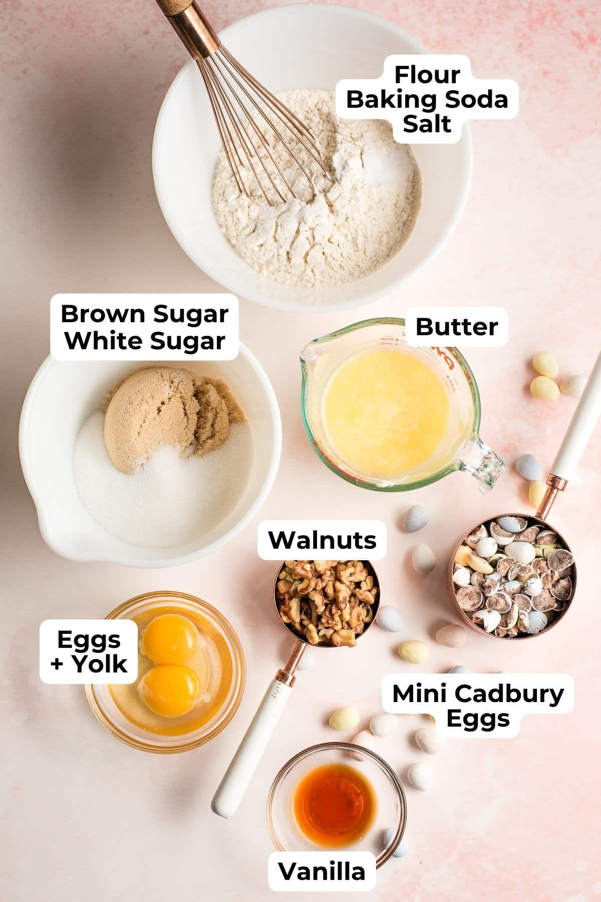 Flour, baking soda, and salt in a bowl, surrounded by bowls of sugar, eggs, melted butter, walnuts, vanilla, and mini Cadbury eggs.