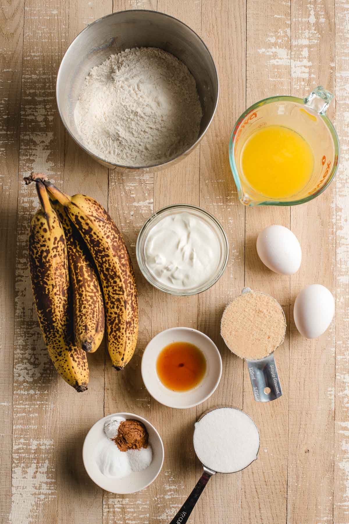 Ingredients for banana bread arranged on a light wood background.