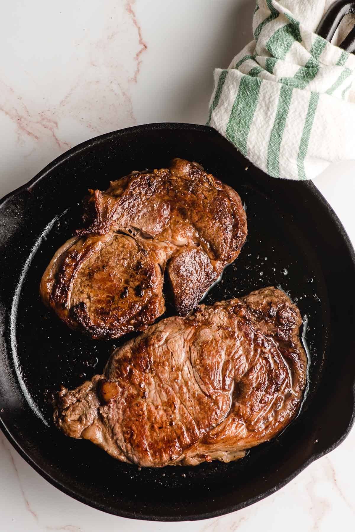 A cast iron skillet with 2 cooked steaks.