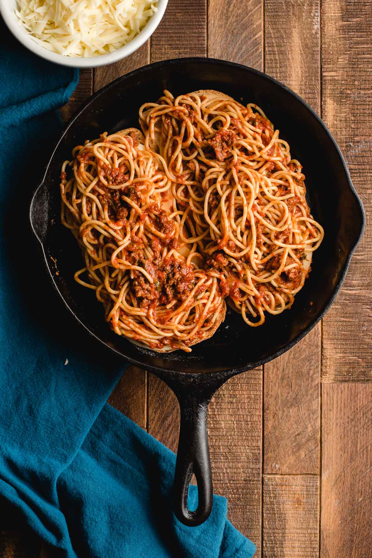Cast iron skillet with two grilled cheeses topped with spaghetti.