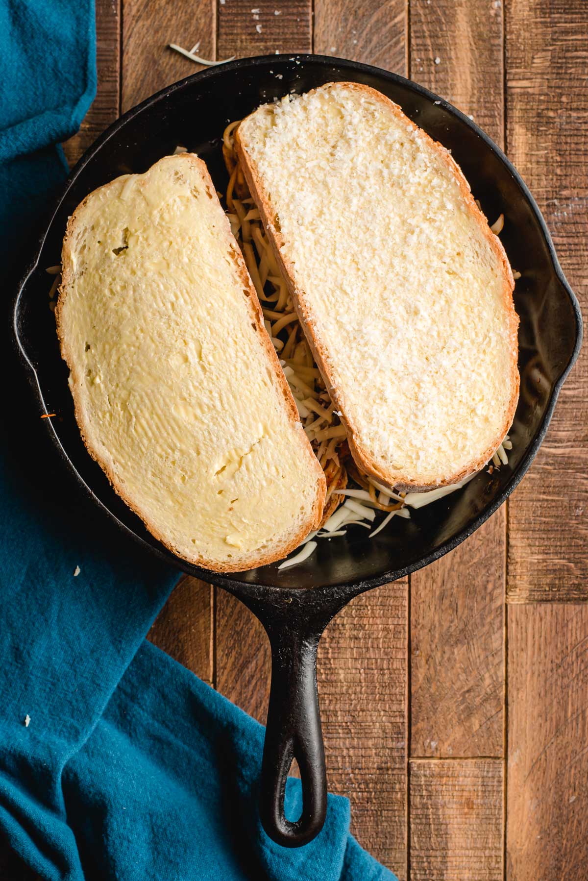 Two grilled cheeses with ungrilled side up in a cast iron skillet.