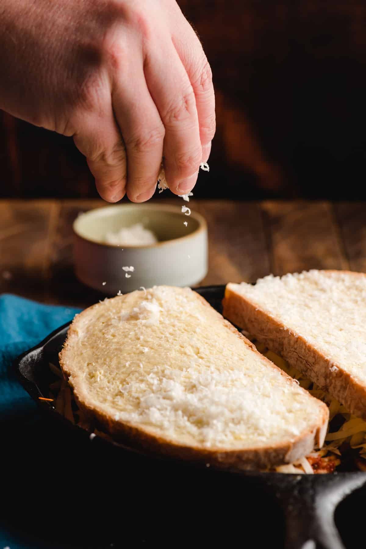 Hand sprinkling parmesan cheese on top of buttered bread.