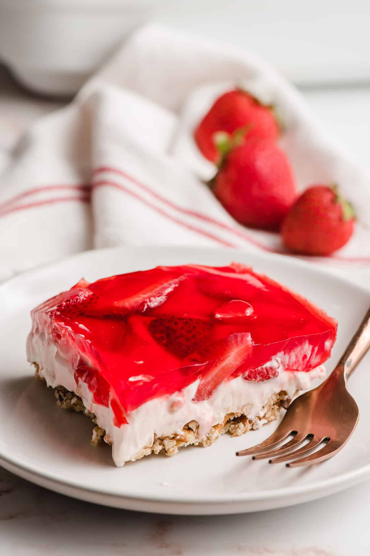 A slice of Strawberry Pretzel Salad on a white plate with a gold fork.