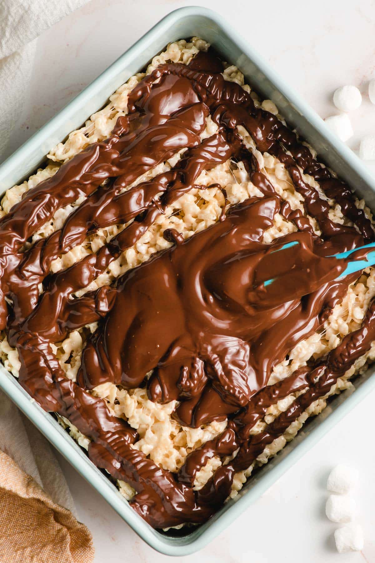 Melted chocolate being spread on a tray of rice krispie treats.