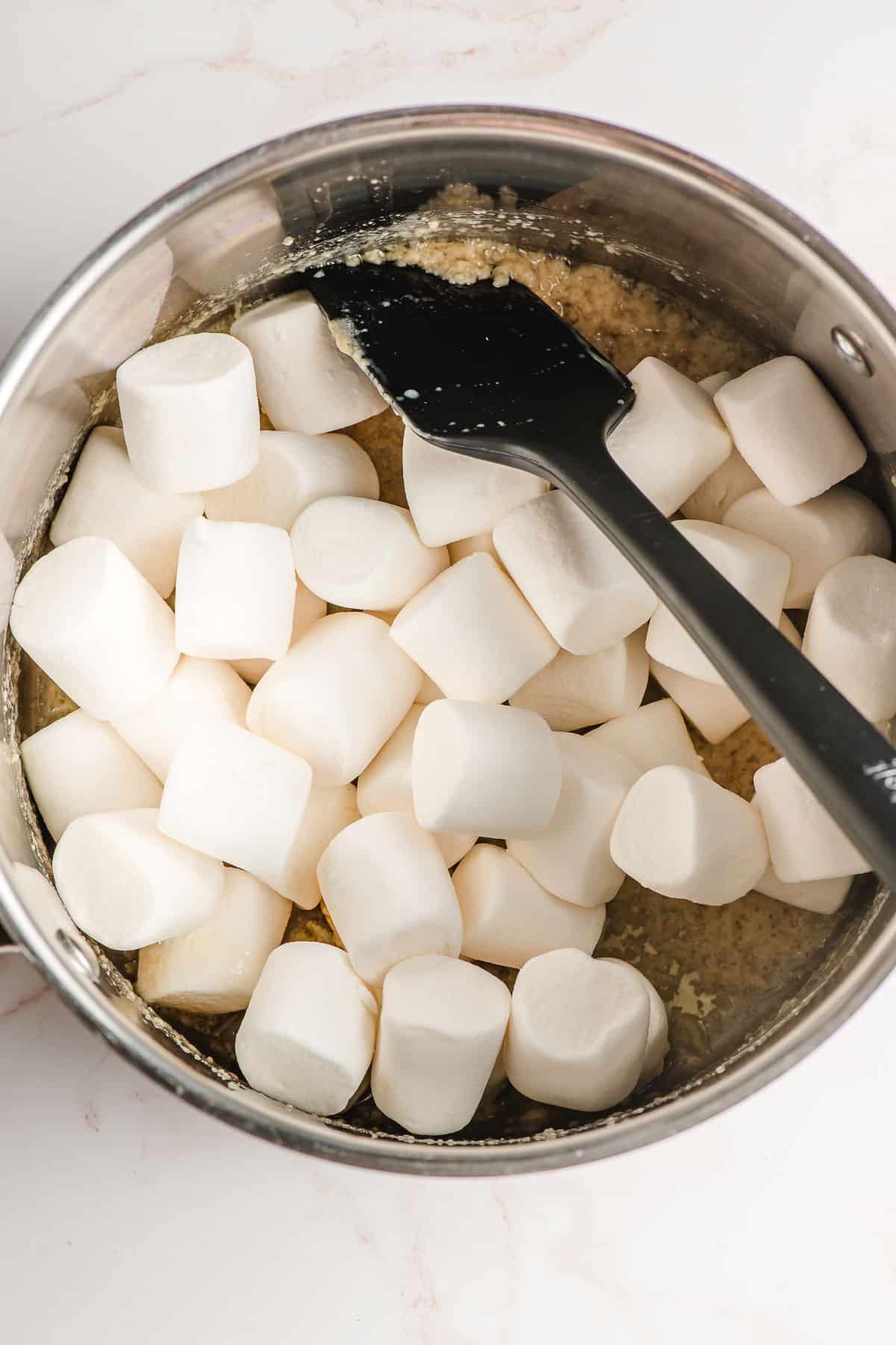 Spatula stirring big marshmallows and butter together in a pot.