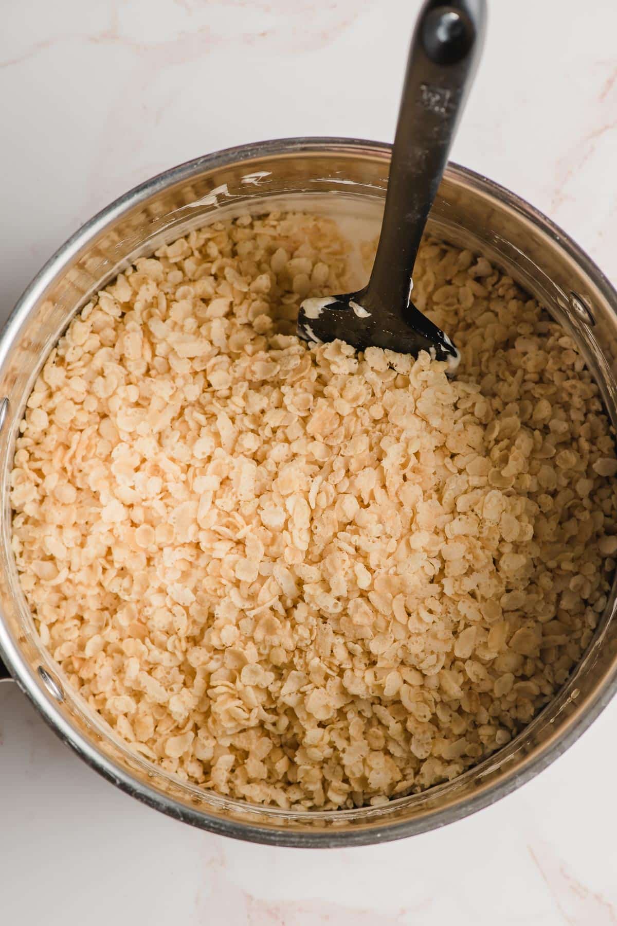 Rice krispies cereal being stirred into melted marshmallows.