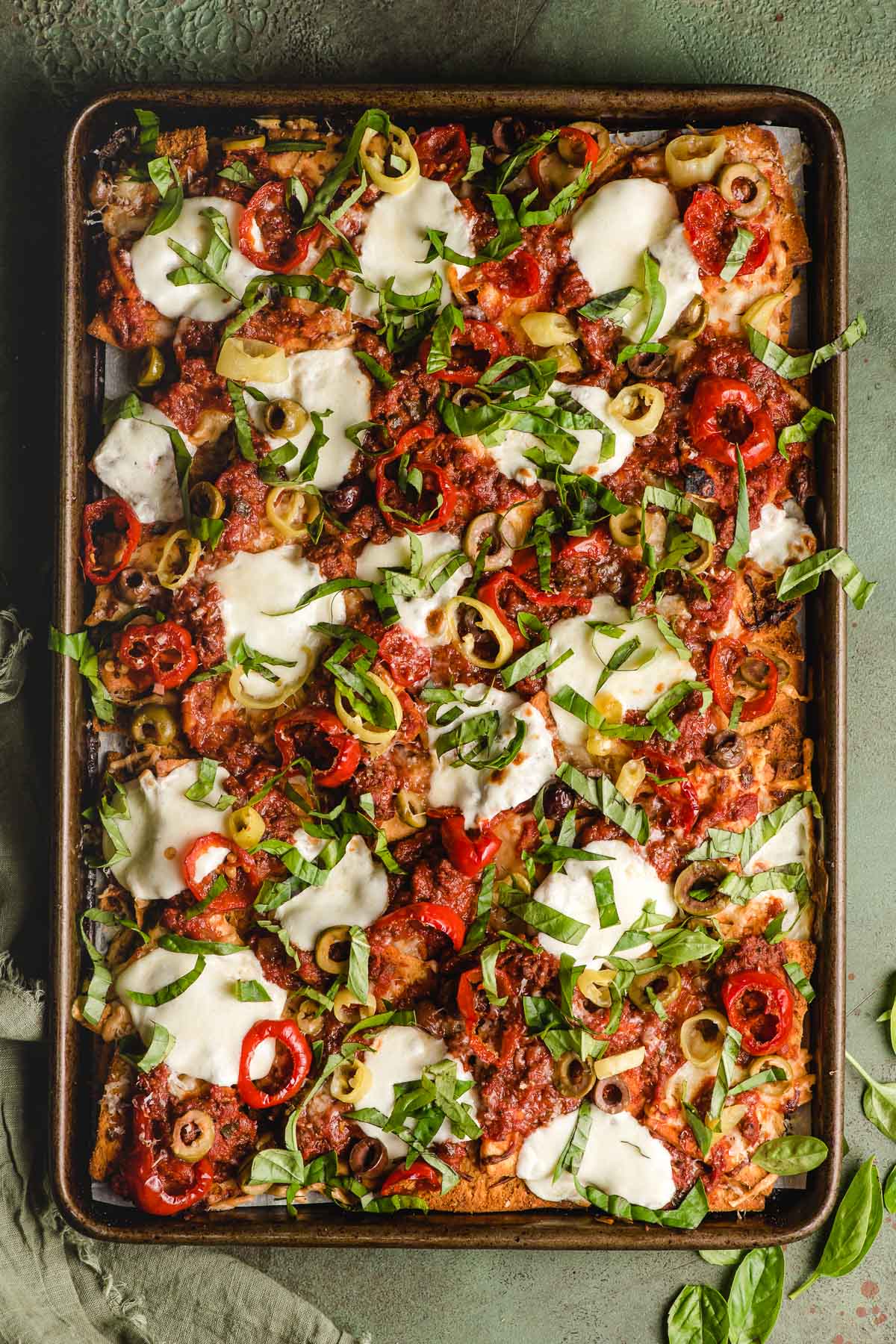 Sheet pan of baked Italian Nachos with sliced melty mozzarella, banana peppers, and olives.