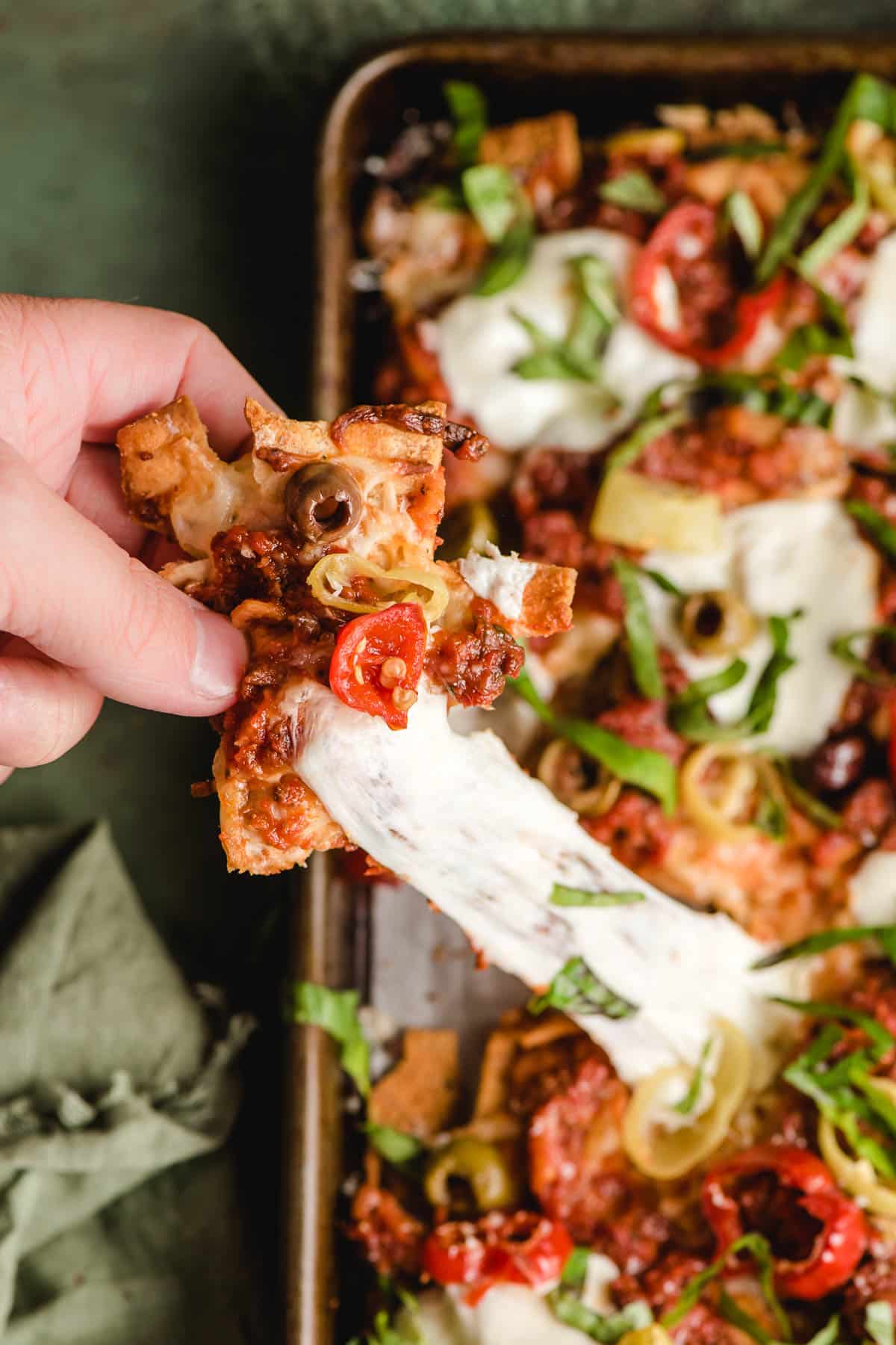 Hand pulling an Italian Nacho off the pan with a string of melted mozzarella left behind.