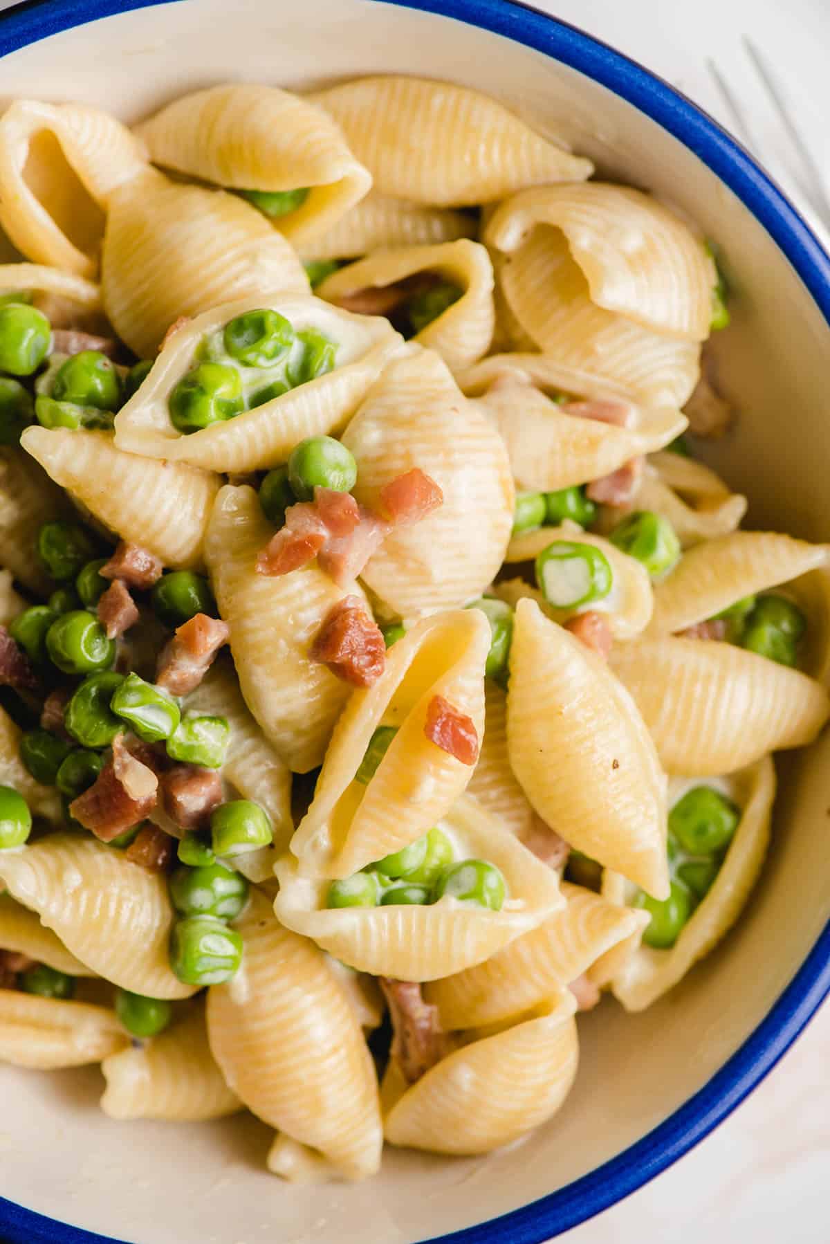 Pasta with peas and pancetta in a blue rimmed bowl.