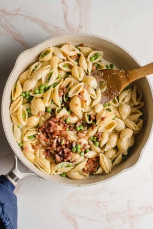 Large skillet with pasta, peas, and pancetta in a cream sauce.