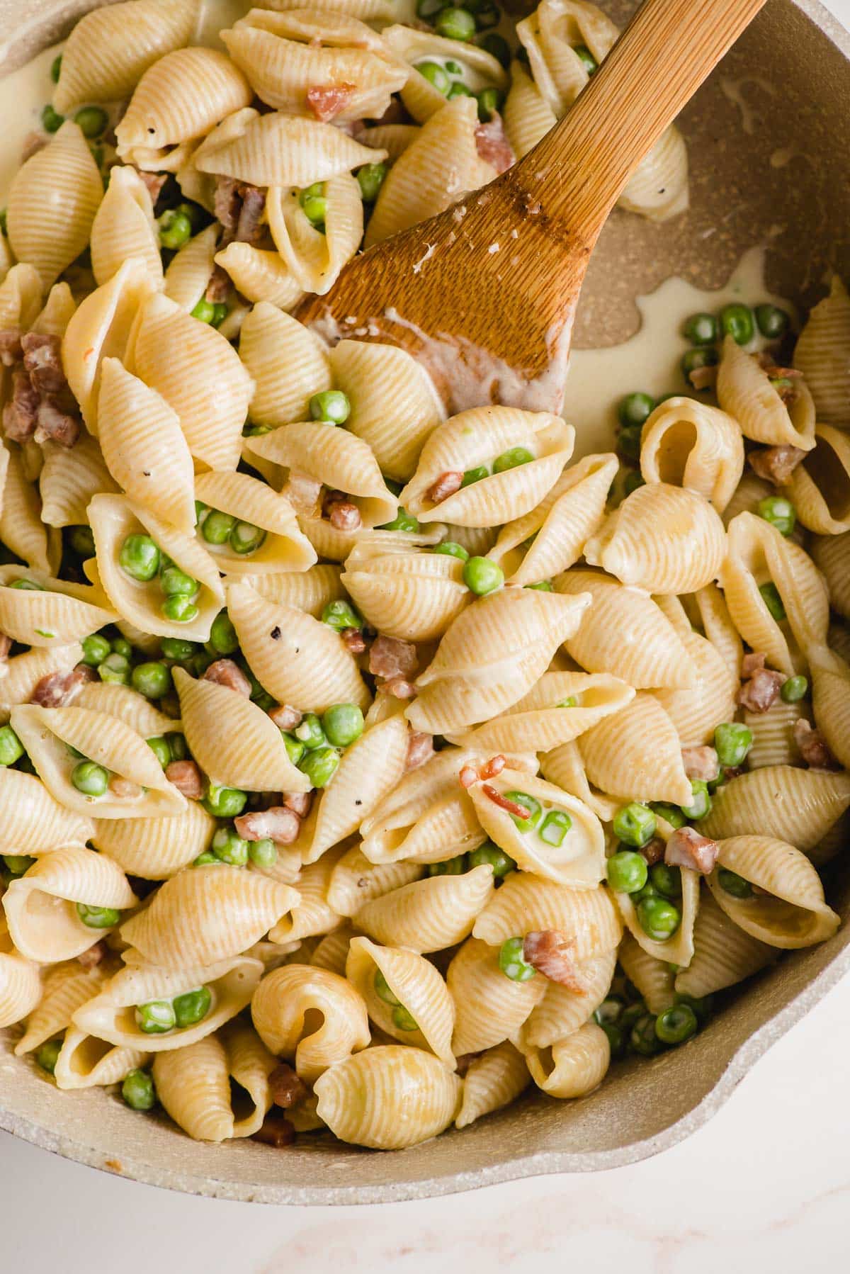 Pasta and peas stirred together by a wooden spoon.