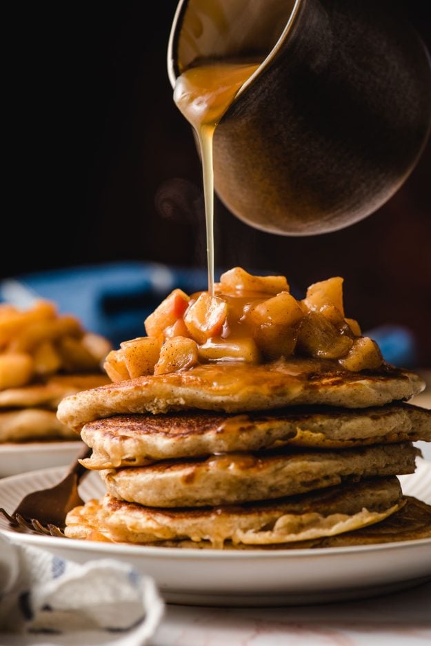 Stack of Apple Cinnamon Pancakes with cider syrup being poured on top.